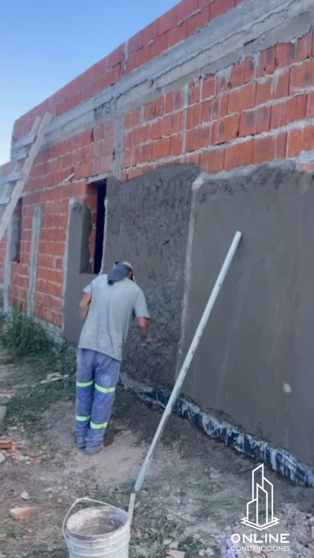 Operario de Online Construcciones aplicando revoque grueso sobre un muro de ladrillo hueco